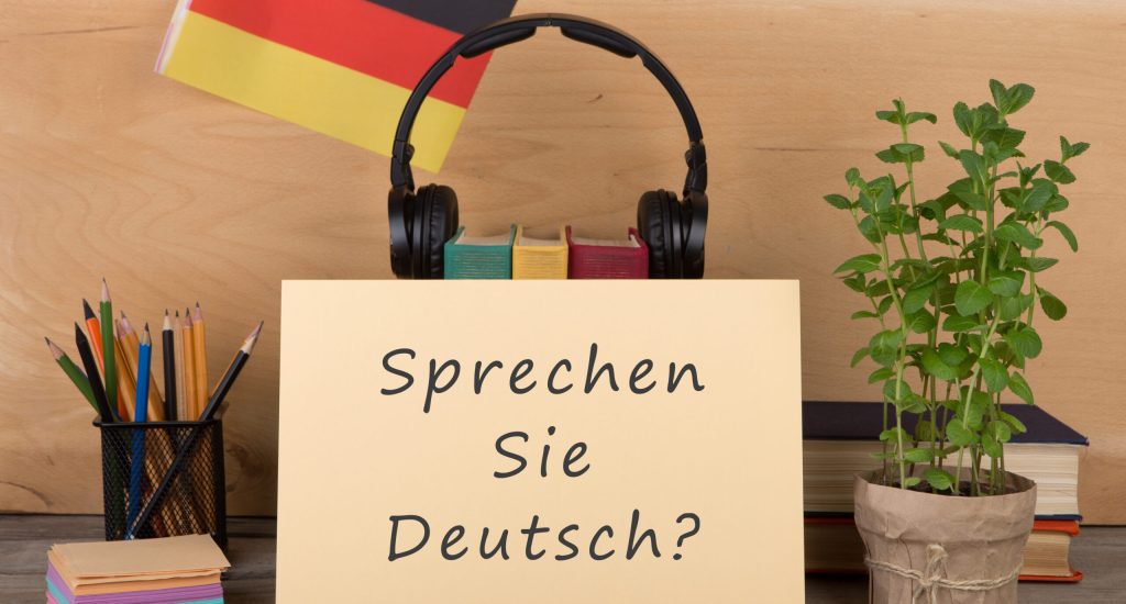 Learning languages concept - paper with text "sprechen sie deutsch?", flag of the Germany, books, headphones, pencils on wooden background